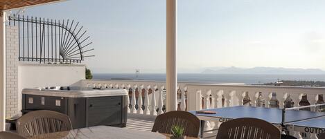A rooftop terrace with a hot tub, outdoor seating, and a scenic view of the sea and mountains.