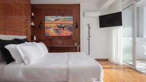 A bedroom with a bed, wooden wardrobe, a painting, a TV, and a sliding glass door. - Athenian Secret Glyfada (Glyfada)