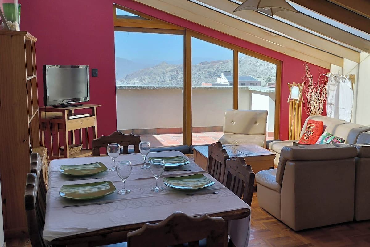 A dining area with a table set for four, a sofa, and a television on a wooden stand.