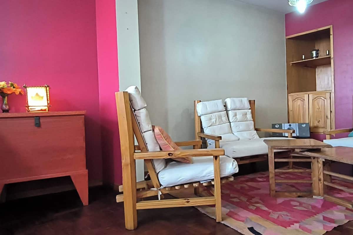 A room with a wooden sofa, a small table, and a cabinet against a pink wall.