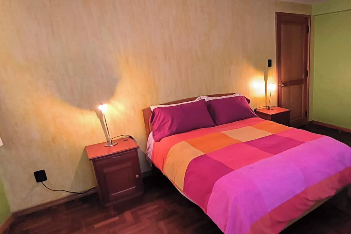 A bedroom with a bed, two bedside tables, a nightstand, a wooden wardrobe, and a green wall.