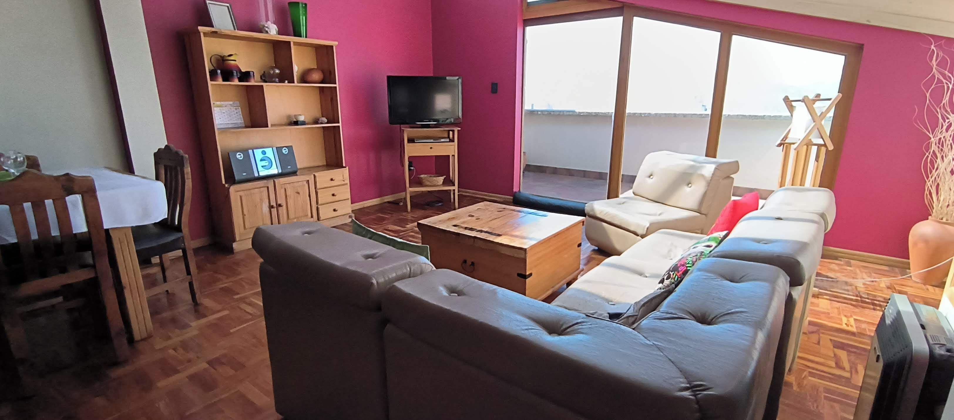 Una sala de estar con un sofá, una mesa de centro, un televisor y una estantería.