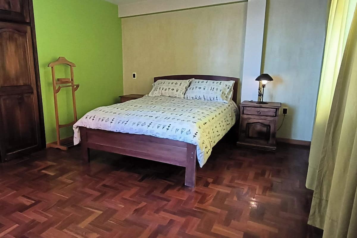 A bedroom with a wooden bed, a nightstand, a wooden wardrobe, and a green wall.