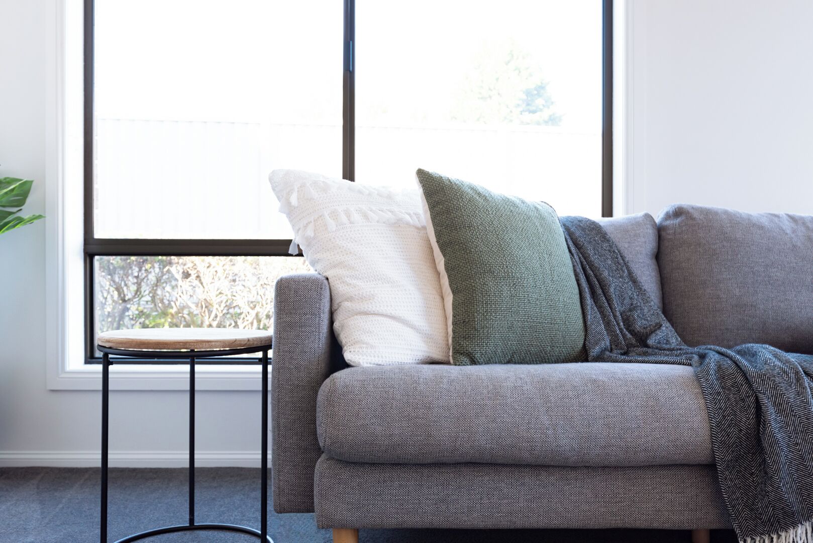 A grey sofa with a woven texture, accompanied by a white and a green pillow, and a grey throw blanket.