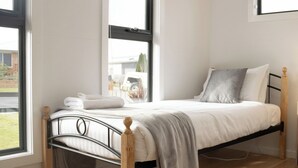 A single bed with a wooden frame and metal headboard, a grey blanket, and a grey pillow.