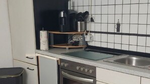 A compact kitchen with white cabinets, a stainless steel sink, a built-in oven, and a coffee maker on the countertop.