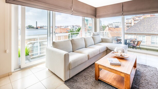 A modern living room with a sofa, a coffee table, and large windows offering a city view. - Orangerie 202 Close to the Beach and Center (Koksijde)