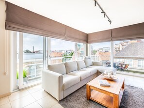 Un salon moderne avec un canapé, une table basse et de grandes fenêtres donnant sur la ville.
