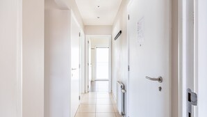 A bright, narrow hallway with white walls and a tiled floor, leading to a door at the end. - Orangerie 202 Close to the Beach and Center (Koksijde)