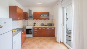 Eine kleine Küche mit Holzausstattung, einem weißen Kühlschrank, einem Herd, einem Backofen und einer Mikrowelle.