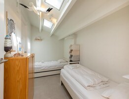 Un dormitorio con dos camas, un aparador de madera, un estante en la pared y un tragaluz.