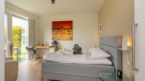 A modern bedroom with a bed, bedside table, and a painting on the wall. - Holiday Home in Nieuwvliet Near the Beach (Nieuwvliet)