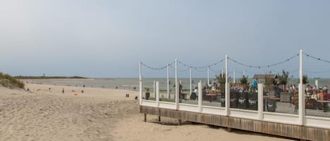 A beach with a wooden boardwalk and a covered seating area with tables and chairs.