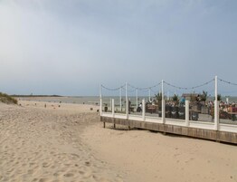 Una playa con un paseo marítimo de madera y un área cubierta con mesas y sillas.