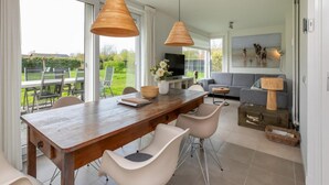 A modern dining area with a wooden table, white chairs, and pendant lights. - Holiday Home in Nieuwvliet Near the Beach (Nieuwvliet)