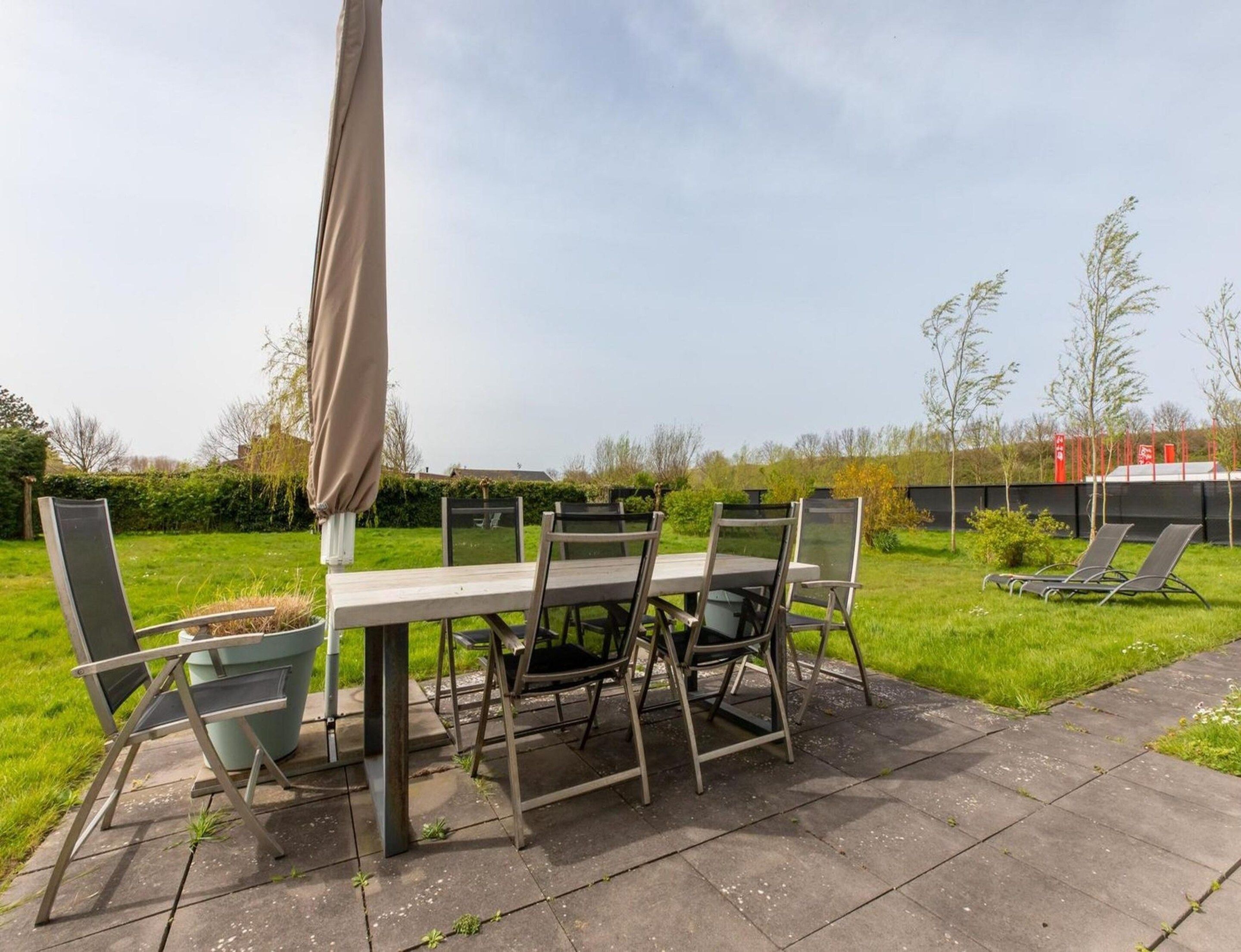 Eine Terrasse im Freien mit Tisch und Stühlen, einem Sonnenschirm und einem Rasenbereich mit Bäumen.