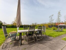 Un patio al aire libre con una mesa y sillas, una sombrilla cubierta y un césped con árboles.