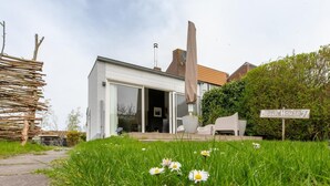 A modern house with a glass door entrance, a patio with outdoor furniture, and a sign indicating 'Beach House 97'. - Holiday Home in Nieuwvliet Near the Beach (Nieuwvliet)