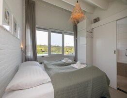 A room with two beds, a window with a view of the outside, a hanging light fixture, and a door.