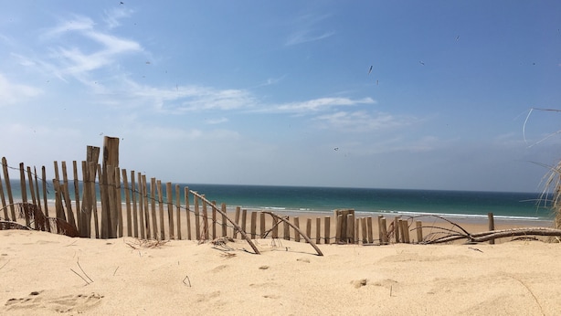 Une plage de sable avec une clôture en bois et des empreintes de pas dans le sable.