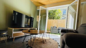 Un salon équipé d’un téléviseur à écran plat, d’une table basse ronde, d’un canapé et offrant une vue sur l’extérieur grâce à une porte vitrée.