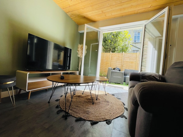 A living room with a flat-screen TV, a round coffee table, a sofa, and a view of the outside through a glass door.