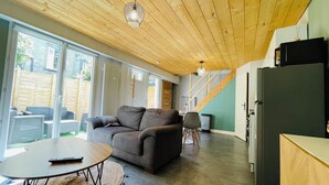 Un salon moderne avec un plafond en bois, un canapé gris, une table ronde et une grande fenêtre.