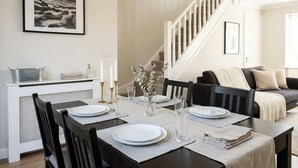 A dining area with a table set for four, a staircase, a sofa, and a framed picture on the wall. - Elegant 3BR Knightsbridge Residence near Harrods (London)