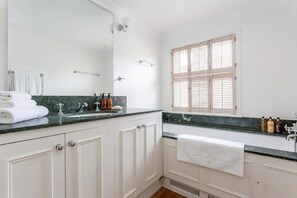 A bathroom with a large mirror, a sink with a faucet, a towel rack, and a window with blinds. - Elegant 3BR Knightsbridge Residence near Harrods (London)