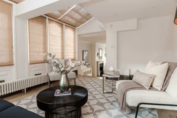 A modern living room with a round black coffee table, a white sofa, and a beige armchair. There is a vase with flowers on the coffee table.