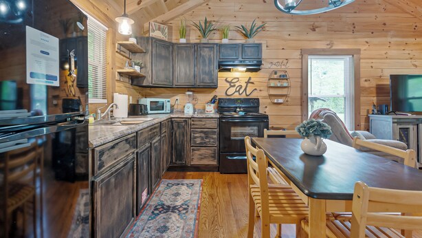 A modern kitchen with dark wood cabinets, a built-in microwave, and a dining area with wooden chairs and a table. - Creek Front Cabin in Pearisburg (Pearisburg)