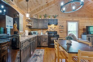 A modern kitchen with dark wood cabinets, a built-in microwave, and a dining area with wooden chairs and a table. - Creek Front Cabin in Pearisburg (Pearisburg)