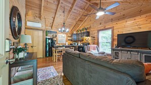 A cozy cabin interior with a wooden ceiling, a sofa, a television, and a kitchen area. - Creek Front Cabin in Pearisburg (Pearisburg)