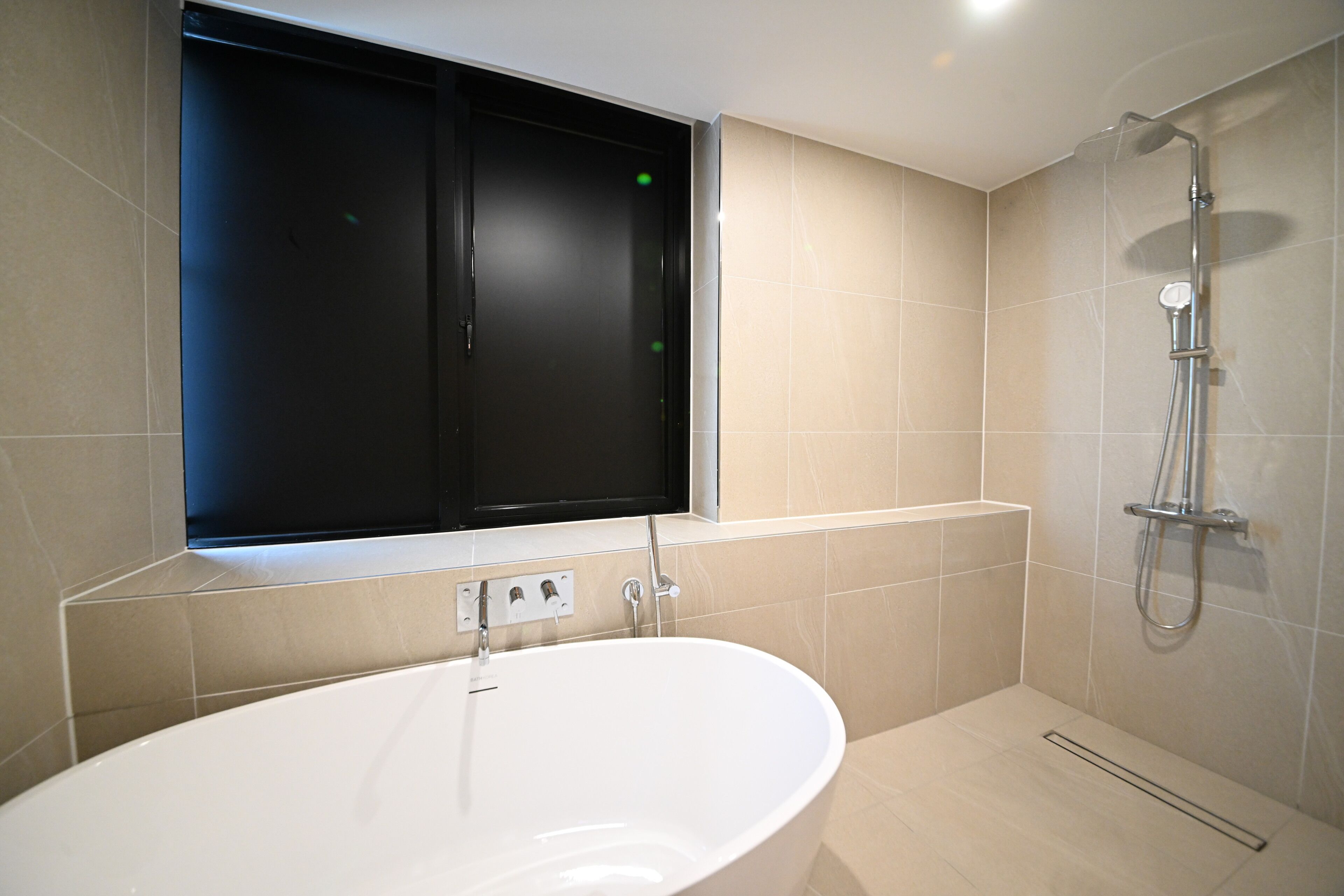 Un baño moderno con una bañera independiente, ducha y ventana con marco negro.