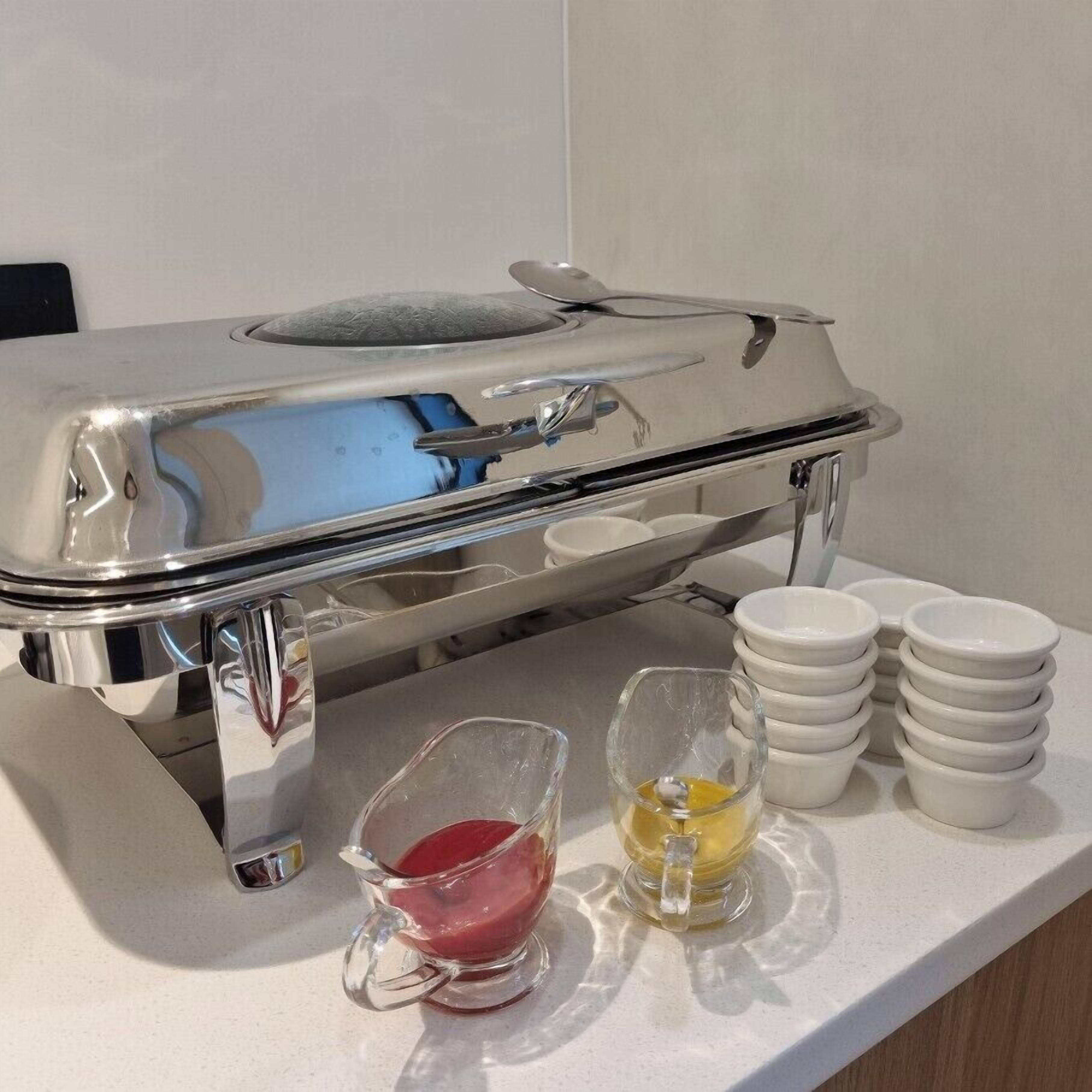Disposición de un bufé con una bandeja de acero inoxidable, un recipiente de vidrio con salsa roja, un recipiente de vidrio con salsa amarilla y varios cuencos blancos apilados sobre el mostrador.