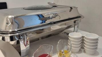 Disposición de un bufé con una bandeja de acero inoxidable, un recipiente de vidrio con salsa roja, un recipiente de vidrio con salsa amarilla y varios cuencos blancos apilados sobre el mostrador.