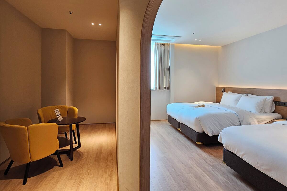 A hotel room with two beds, a small table, and a yellow chair.