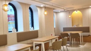 Un interior de restaurante moderno con mesas y sillas de madera, ventanas amplias con arcos y lámparas colgantes.
