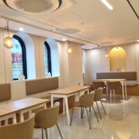 Un interior de restaurante moderno con mesas y sillas de madera, ventanas amplias con arcos y lámparas colgantes.