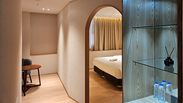 Una habitación de hotel moderna con una cama, una mesita y un mueble de vidrio con botellas de agua.