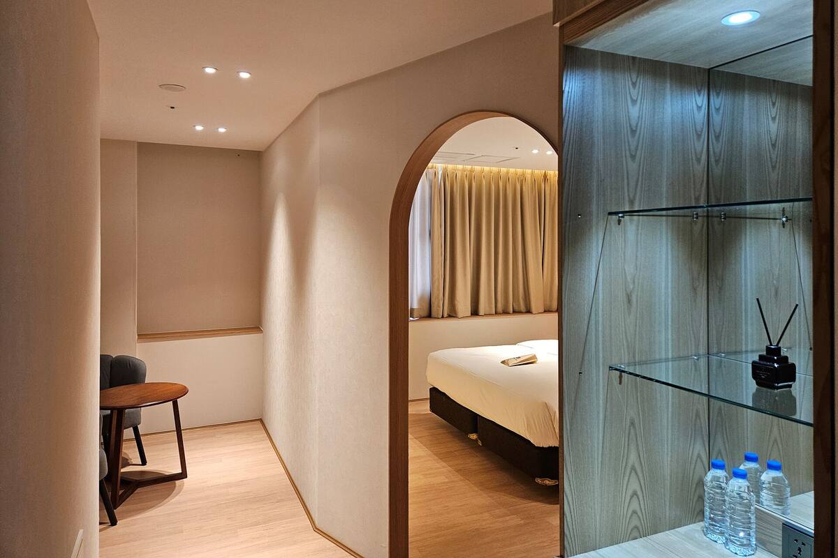A modern hotel room with a bed, a small table, and a glass cabinet with water bottles.