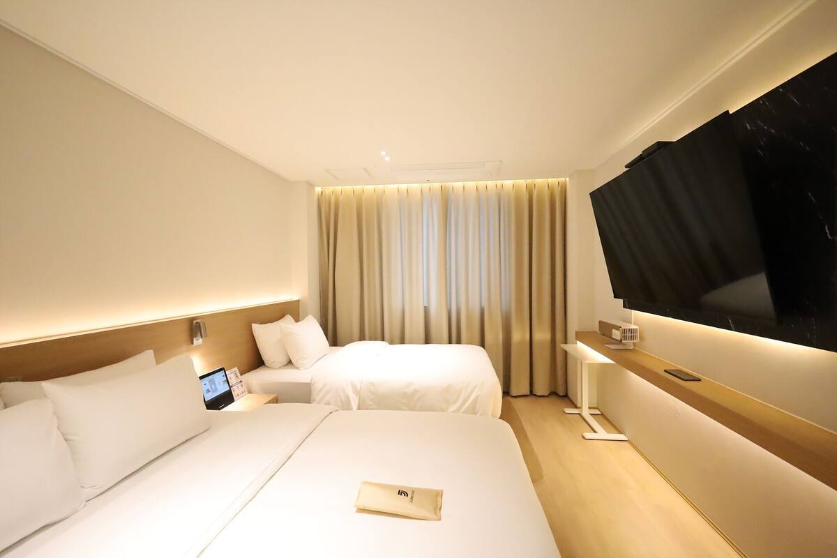 A hotel room with a large bed, a smaller bed, a TV, and a desk with a computer.
