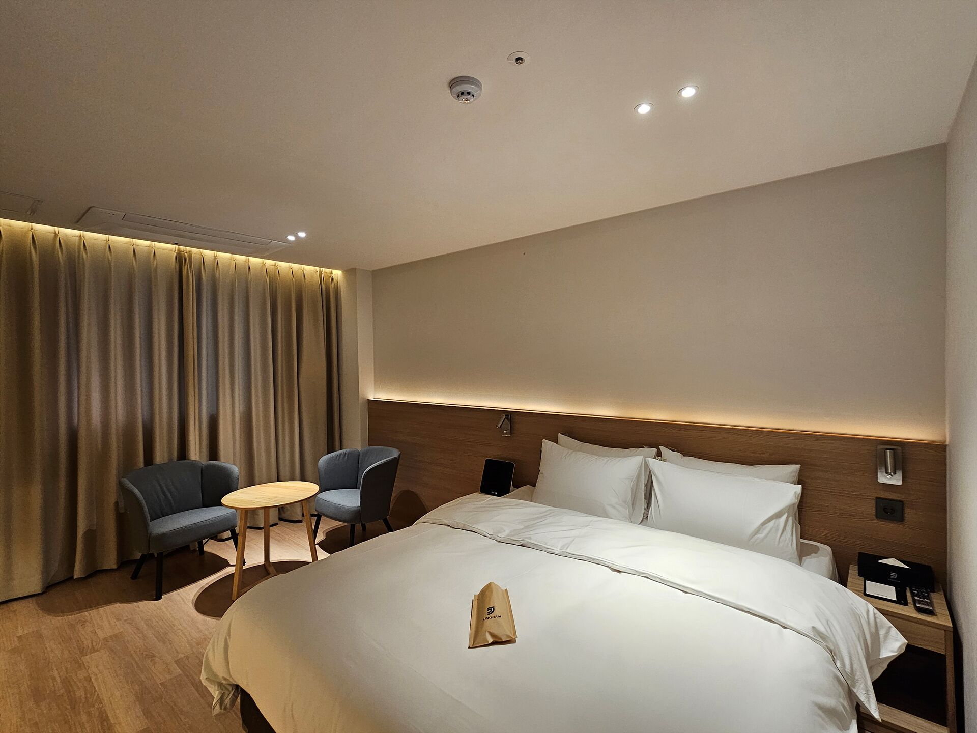 A modern hotel room with a large bed, two chairs, a small table, and a curtain.