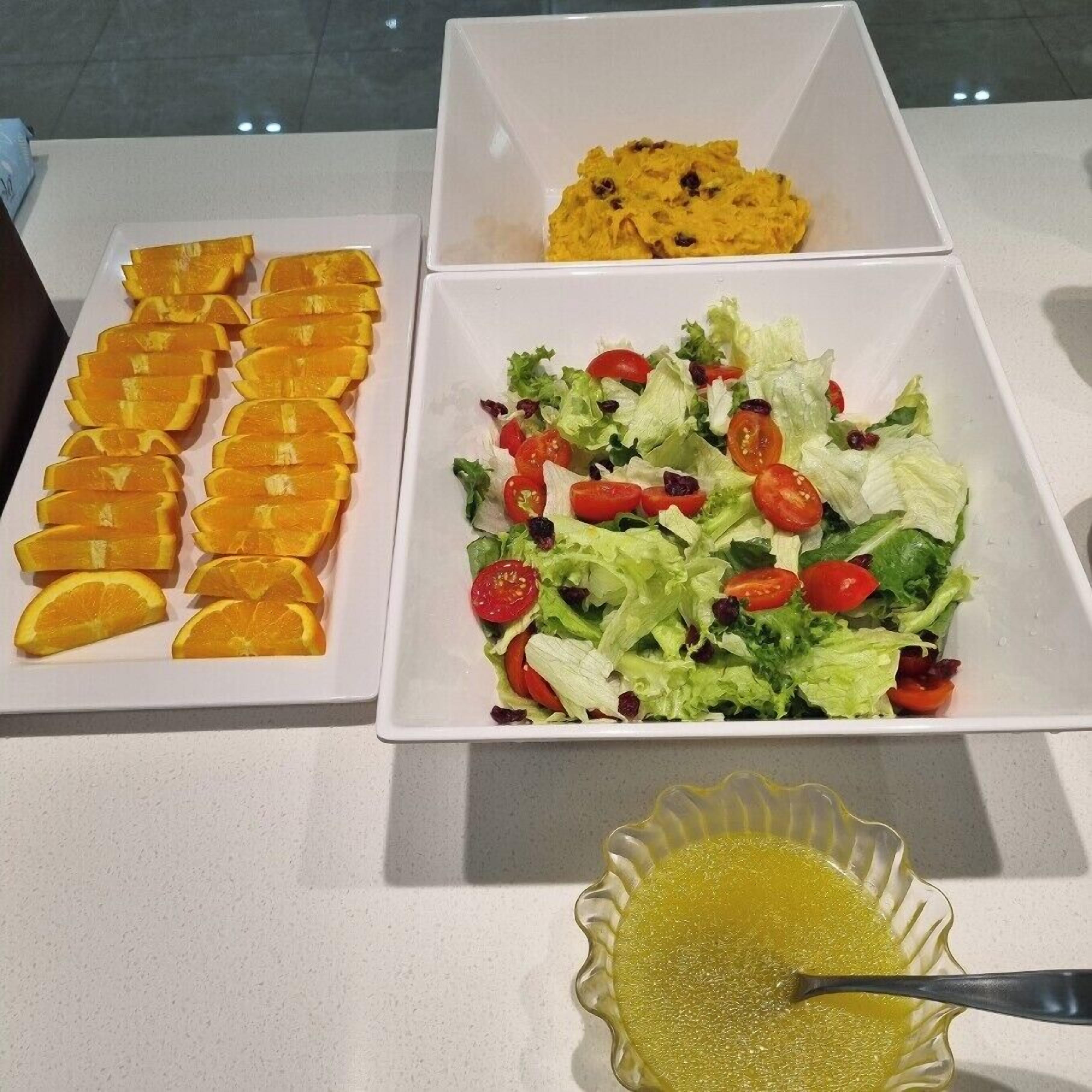 Una mesa con tres platos: rodajas de naranja, una ensalada de lechuga y tomates cherry, y un tazón de sopa amarilla.