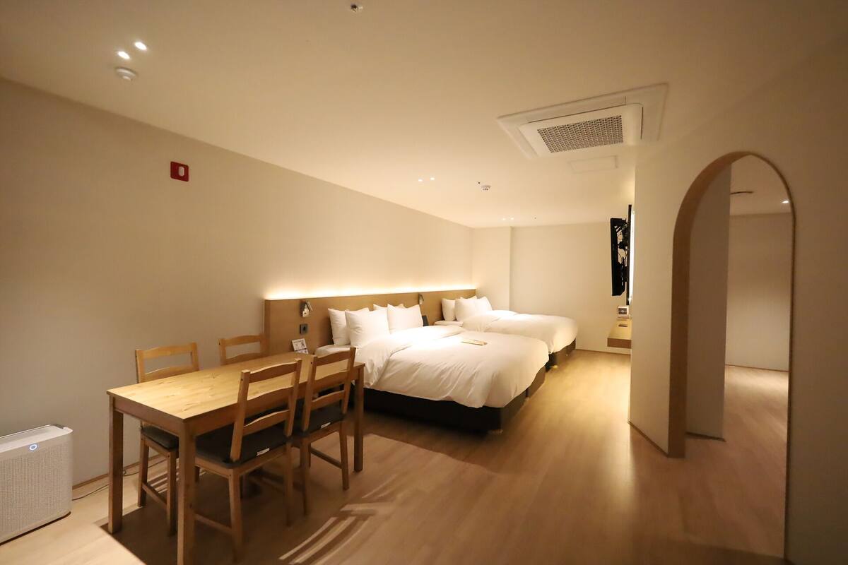 A hotel room with a wooden dining table, two beds, and a modern design.