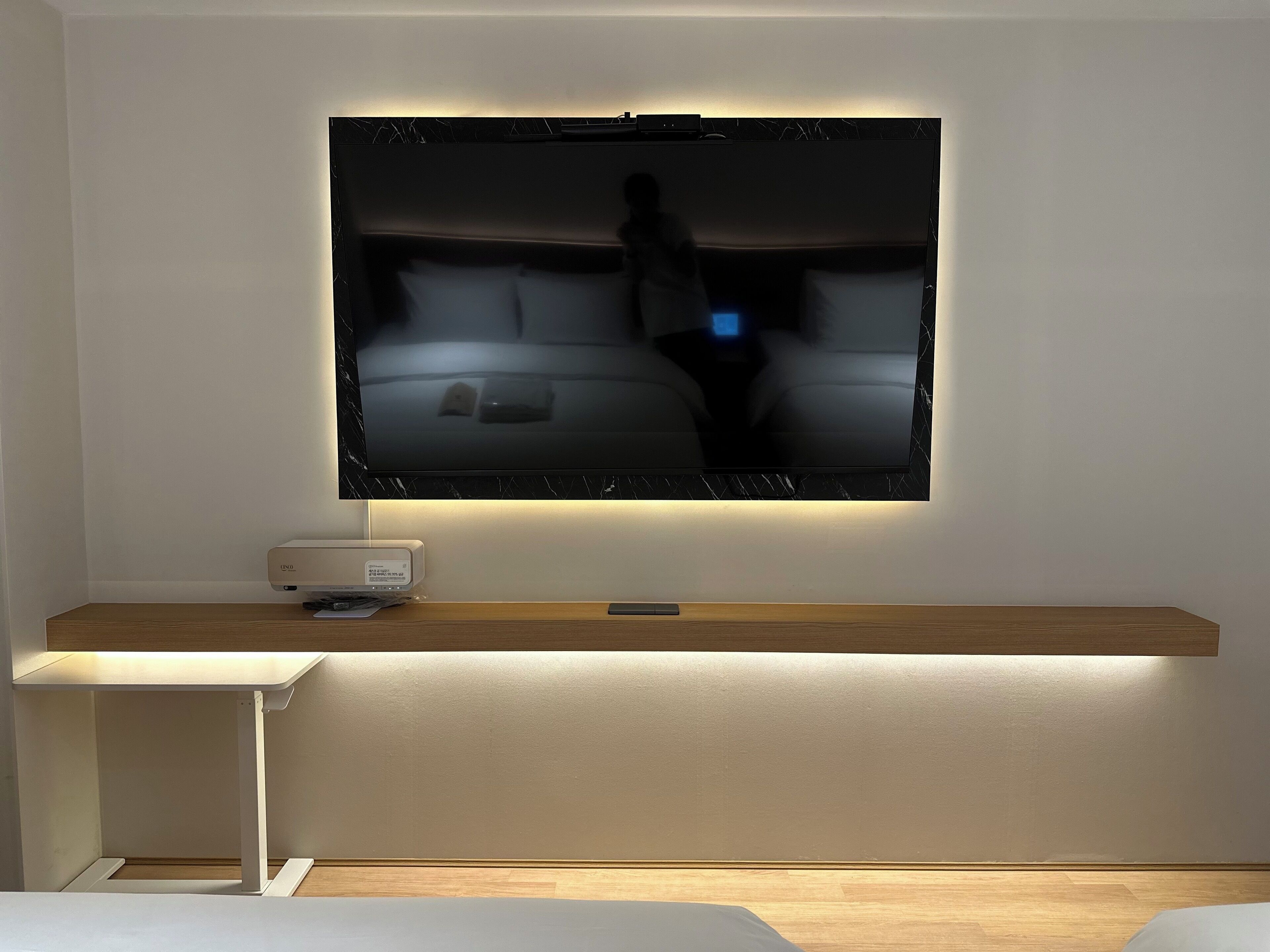 A flat-screen TV mounted on a wall with a wooden shelf below.