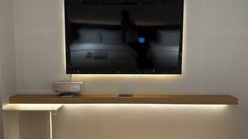 A flat-screen TV mounted on a wall with a wooden shelf below.