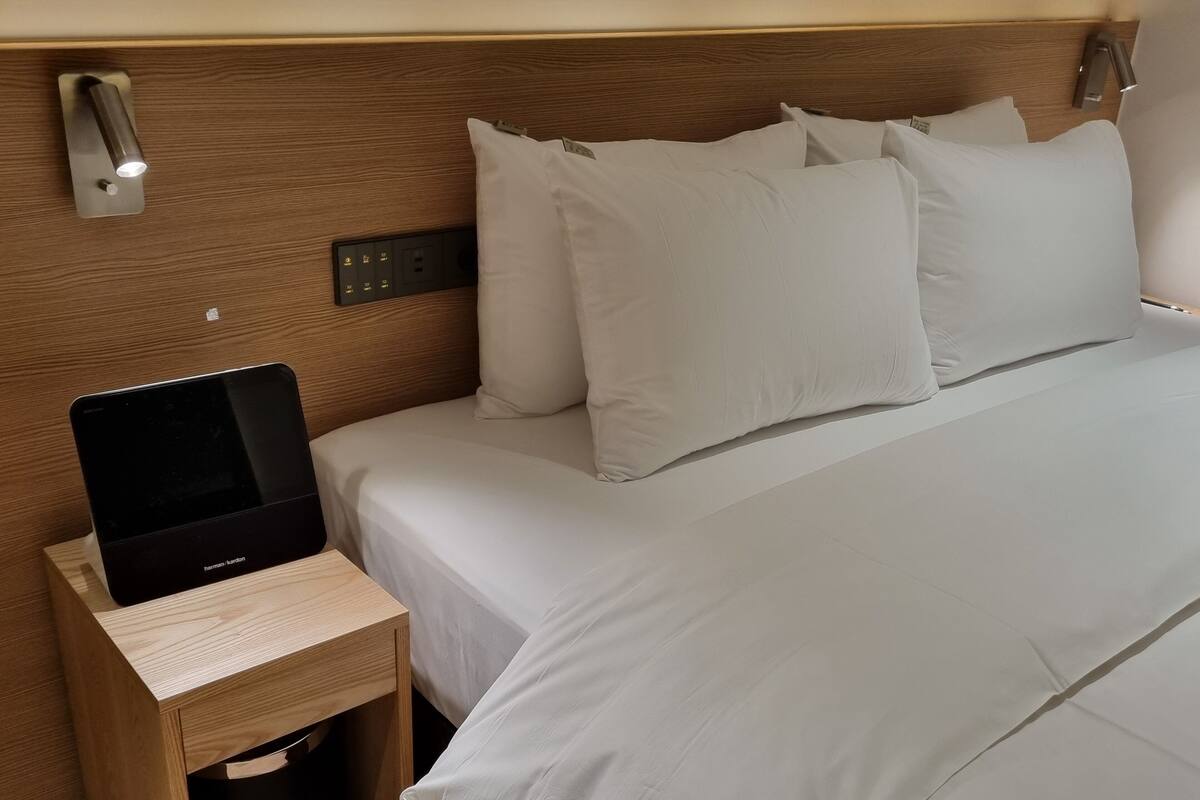 A neatly made bed with white linens, a bedside table with a laptop, and a wall-mounted light fixture.