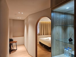 Una habitación de hotel moderna con una cama, una mesita y un mueble de vidrio con botellas de agua.