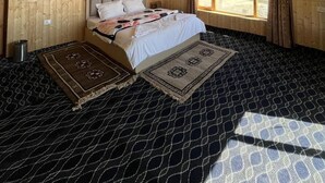 A bedroom with a wooden ceiling, a bed with a patterned bedspread, a window with curtains, and a patterned rug.